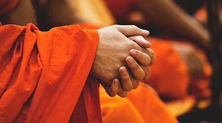 mãos de monge orando, em túnica laranja - Brahmacharya - celibato