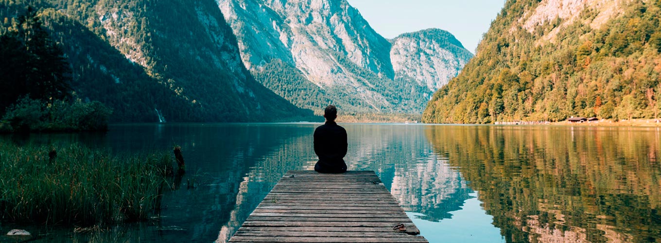 lei do darma: a sétima lei espiritual do sucesso representada por homem sentado a beira de um lago